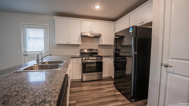 kitchen with a sink, under cabinet range hood, freestanding refrigerator, gas range, and dark wood finished floors