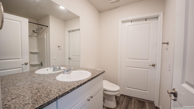 bathroom featuring wood finished floors, toilet, a shower, and vanity