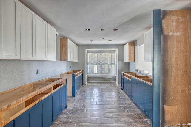 kitchen featuring a textured ceiling, blue cabinets, white cabinets, and dark wood finished floors