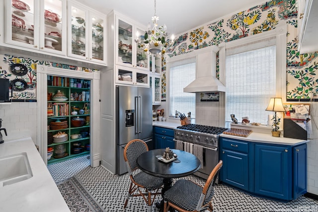 112 King William, San Antonio, TX 78204 - kitchen featuring high end appliances, blue cabinetry, light countertops, premium range hood, and wallpapered walls