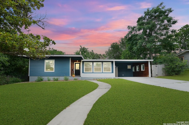view of front facade featuring driveway, fence, a carport, and a yard