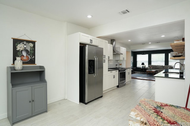 kitchen featuring white cabinets, a sink, appliances with stainless steel finishes, visible vents, and wall chimney exhaust hood