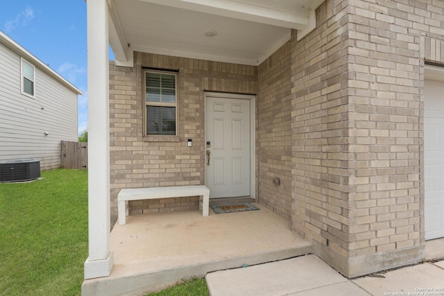 property entrance featuring fence, cooling unit, a yard, and brick siding