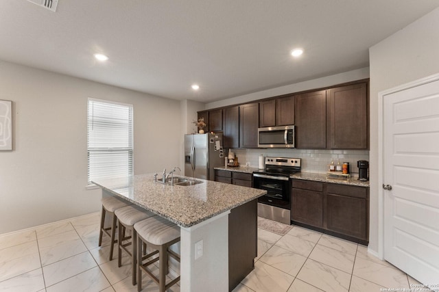 kitchen featuring a sink, a kitchen breakfast bar, marble finish floor, appliances with stainless steel finishes, and an island with sink