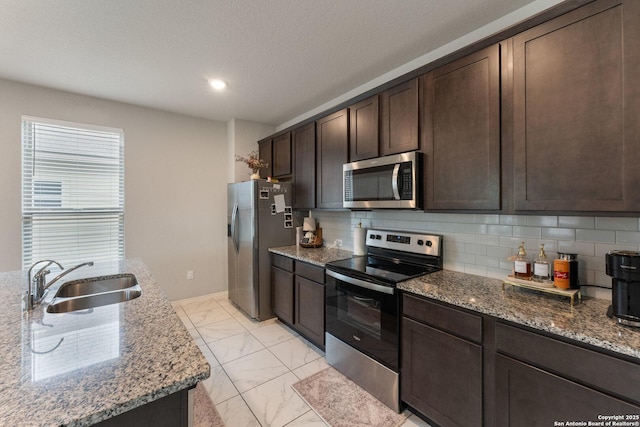 kitchen featuring light stone countertops, appliances with stainless steel finishes, marble finish floor, dark brown cabinets, and a sink