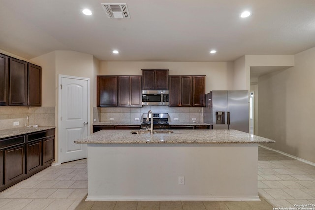 kitchen featuring decorative backsplash, a sink, appliances with stainless steel finishes, light tile patterned flooring, and an island with sink