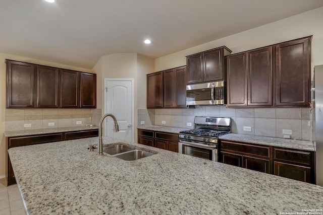 kitchen with light stone countertops, a sink, tasteful backsplash, dark brown cabinetry, and appliances with stainless steel finishes