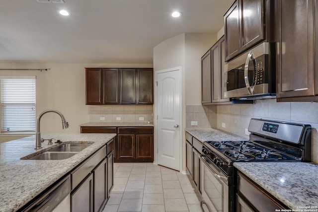 kitchen with a sink, appliances with stainless steel finishes, backsplash, light stone counters, and dark brown cabinets