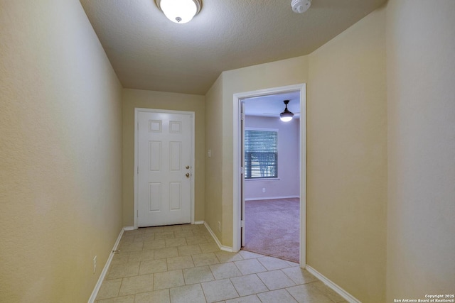 hallway with light tile patterned floors, a textured ceiling, and baseboards