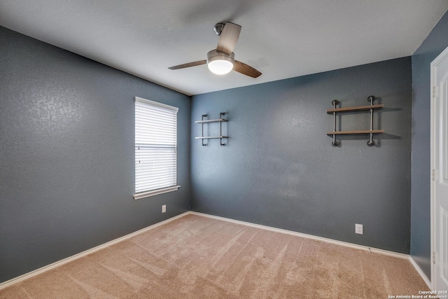 carpeted spare room featuring ceiling fan and baseboards