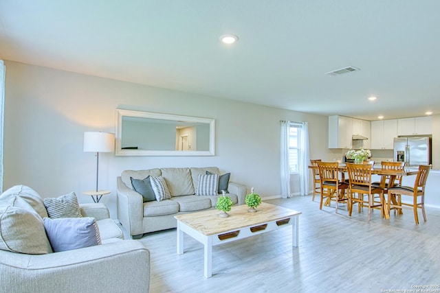 living area with light wood finished floors, recessed lighting, visible vents, and baseboards