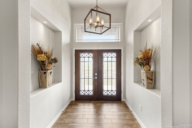 foyer entrance with baseboards, wood finished floors, an inviting chandelier, and french doors