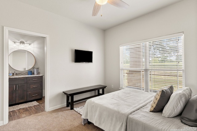 carpeted bedroom featuring a sink, ceiling fan, ensuite bath, and baseboards