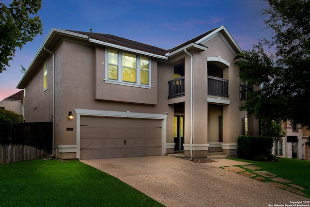 traditional home featuring a balcony, an attached garage, driveway, stucco siding, and fence
