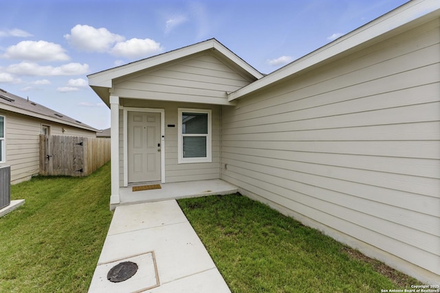 view of exterior entry featuring fence and a lawn