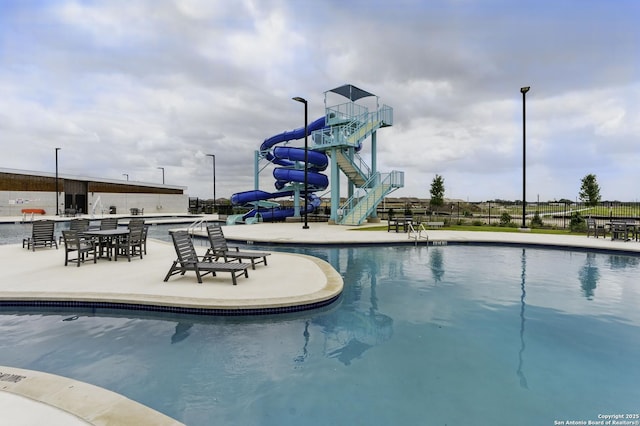 community pool featuring a water slide, a patio, outdoor dry bar, and stairs