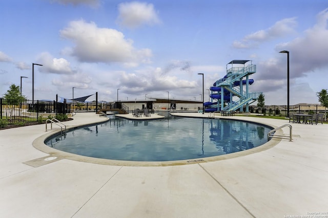 community pool featuring a patio, a water slide, and fence