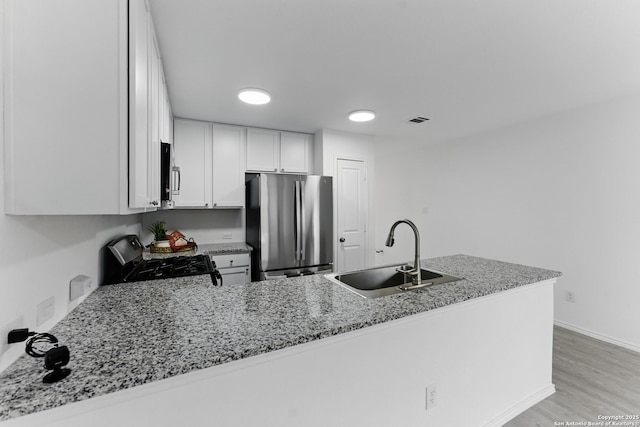 kitchen featuring a sink, stainless steel appliances, visible vents, white cabinetry, and light stone counters