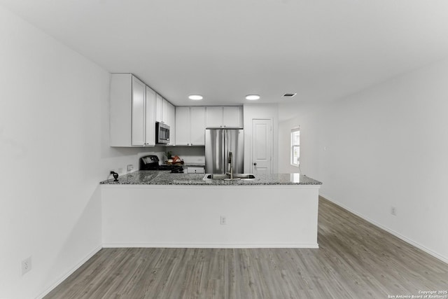 kitchen featuring dark stone counters, white cabinetry, appliances with stainless steel finishes, light wood-style floors, and a peninsula