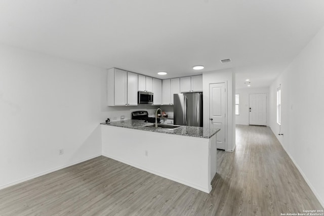 kitchen with a sink, stainless steel appliances, visible vents, a peninsula, and light wood-style flooring