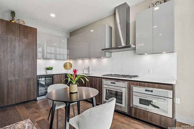 kitchen with modern cabinets, a sink, stainless steel appliances, wine cooler, and wall chimney exhaust hood