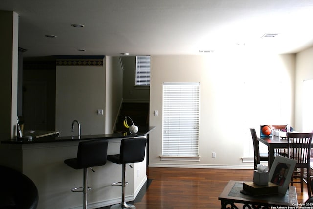 kitchen featuring a breakfast bar, visible vents, baseboards, dark countertops, and dark wood finished floors