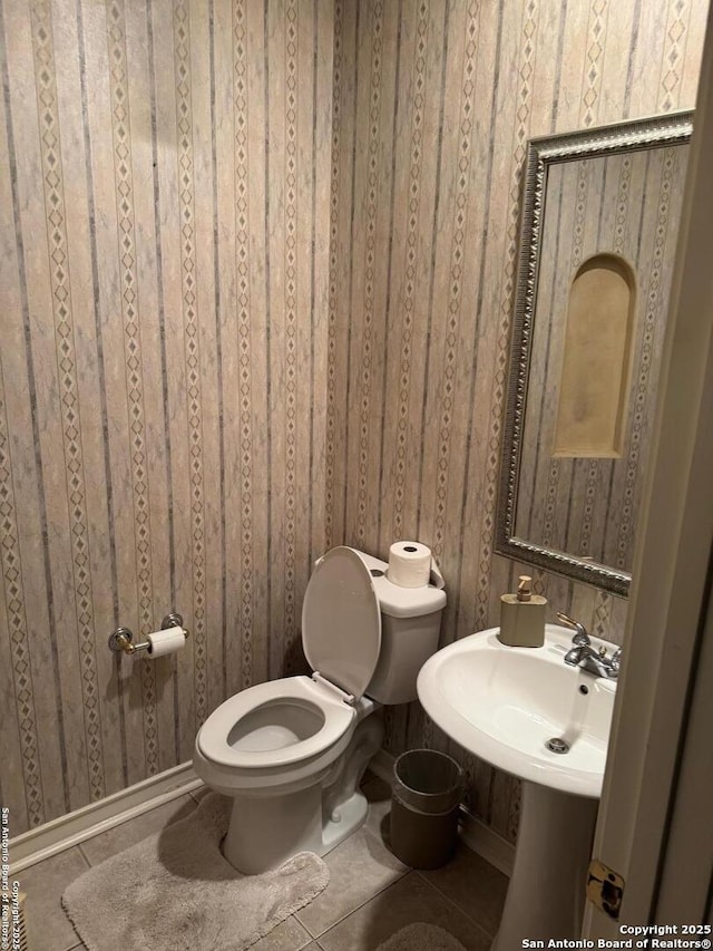 half bathroom featuring wallpapered walls, toilet, tile patterned flooring, and a sink
