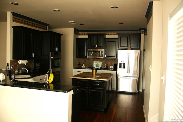 kitchen featuring dark stone countertops, tasteful backsplash, appliances with stainless steel finishes, dark wood finished floors, and a peninsula