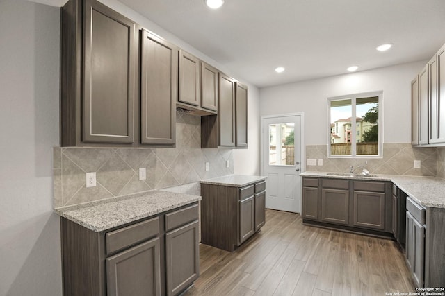 kitchen featuring recessed lighting, light stone counters, decorative backsplash, light wood finished floors, and a sink