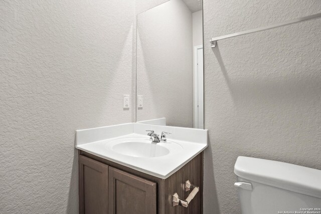 half bath with toilet, a textured wall, and vanity