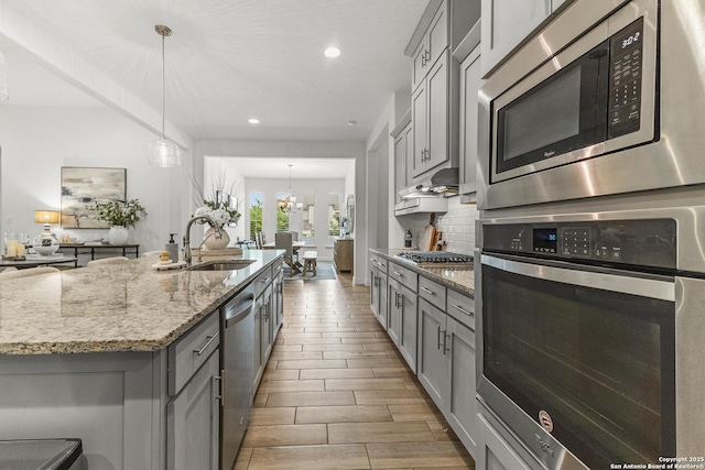kitchen with decorative backsplash, a sink, appliances with stainless steel finishes, light stone countertops, and gray cabinets