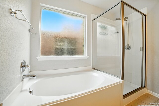bathroom featuring a stall shower, a wealth of natural light, a garden tub, and a textured wall