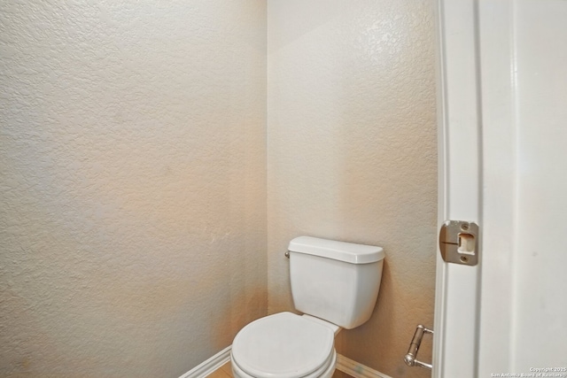 bathroom with toilet, a textured wall, and baseboards