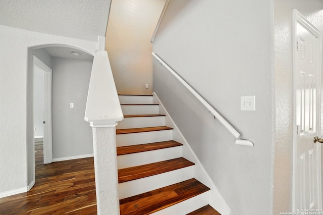 staircase with arched walkways, wood finished floors, and baseboards