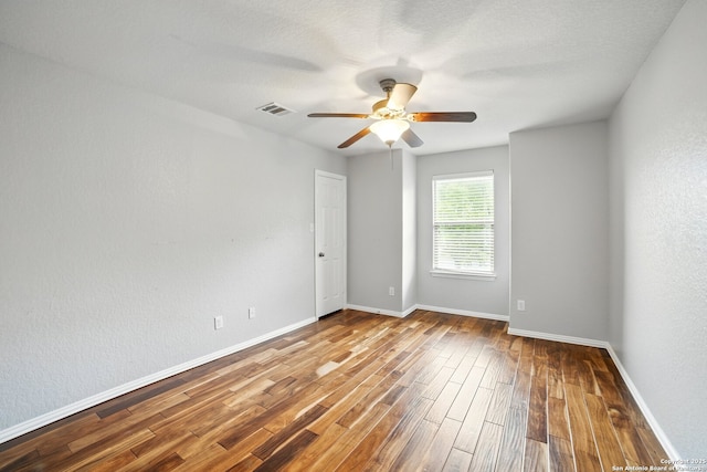 empty room with wood finished floors, visible vents, a ceiling fan, and baseboards