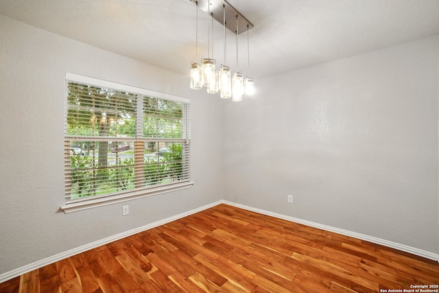 empty room with baseboards, wood finished floors, and an inviting chandelier
