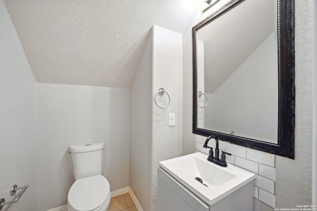 half bathroom featuring toilet, a textured wall, vanity, a textured ceiling, and lofted ceiling