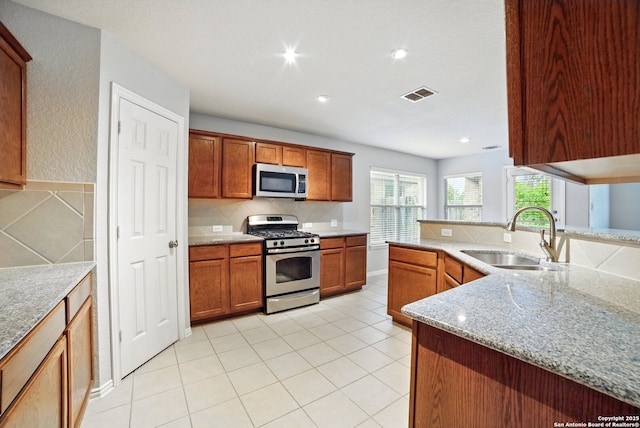 kitchen featuring light stone counters, a sink, visible vents, stainless steel appliances, and backsplash