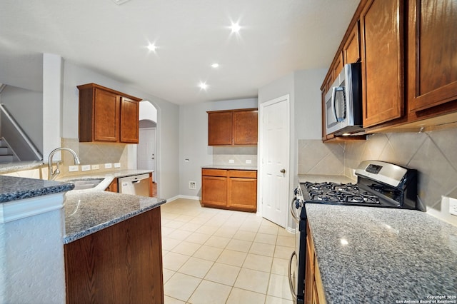 kitchen with dark stone counters, a sink, light tile patterned floors, arched walkways, and appliances with stainless steel finishes