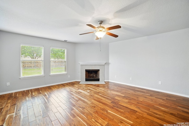 unfurnished living room with a fireplace, wood finished floors, ceiling fan, and baseboards