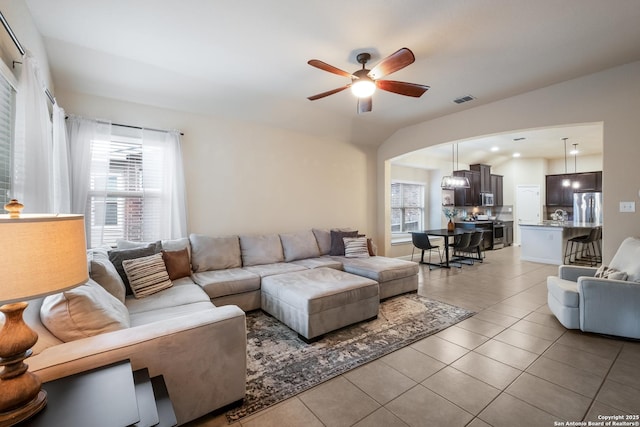 living area with light tile patterned floors, arched walkways, visible vents, and ceiling fan