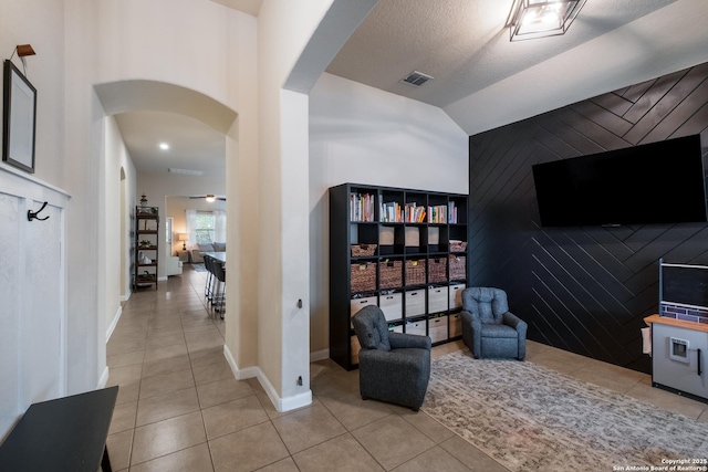 sitting room featuring visible vents, arched walkways, light tile patterned floors, and an accent wall