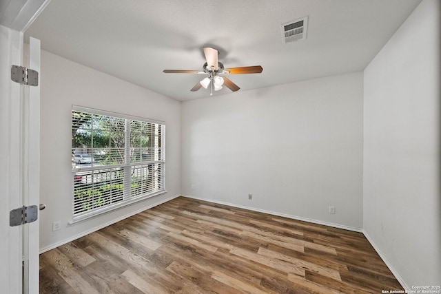 spare room with a ceiling fan, visible vents, wood finished floors, and baseboards