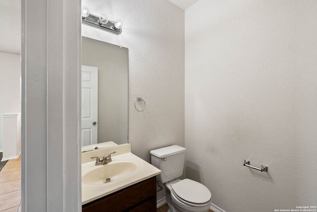 bathroom with toilet, a textured wall, vanity, and tile patterned flooring
