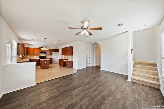 unfurnished living room with stairs, visible vents, arched walkways, wood finished floors, and ceiling fan with notable chandelier