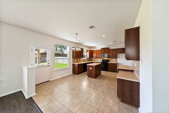 kitchen featuring tasteful backsplash, light countertops, a kitchen island, black appliances, and visible vents