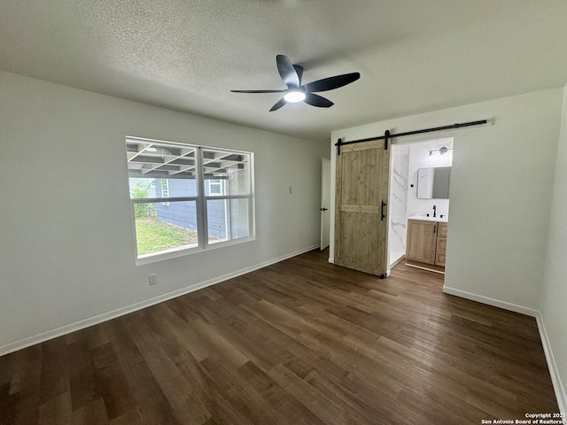 629 Melrose, Seguin, TX 78155 - unfurnished bedroom featuring baseboards, a barn door, connected bathroom, and dark wood-style flooring