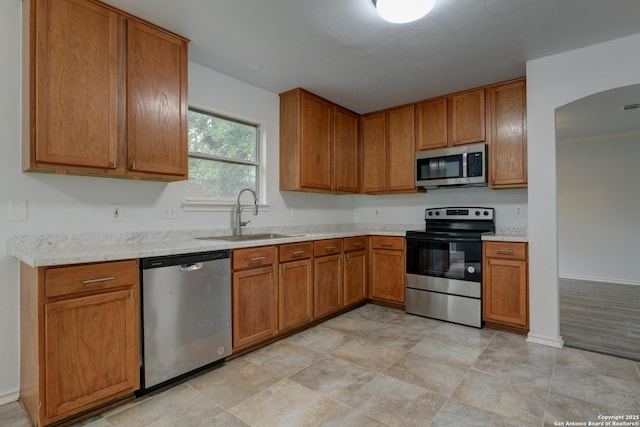6015 Wexford Pl, San Antonio, TX 78240 - kitchen featuring a sink, stainless steel appliances, light countertops, arched walkways, and brown cabinetry