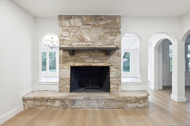 details with wood finished floors, arched walkways, a stone fireplace, and baseboards