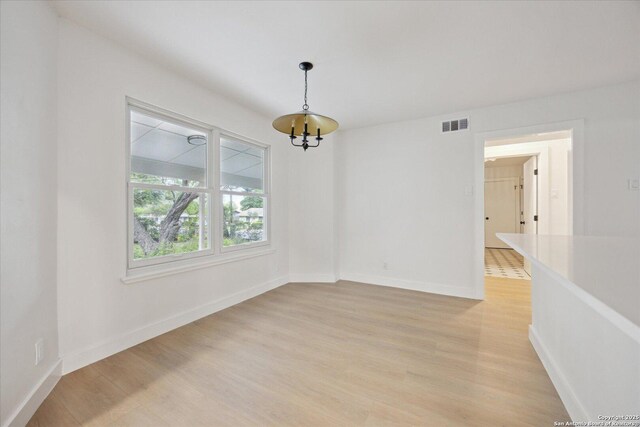 empty room with an inviting chandelier, visible vents, light wood-type flooring, and baseboards